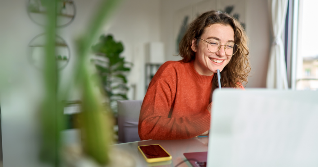 Young happy woman student using laptop watching webinar writing at home